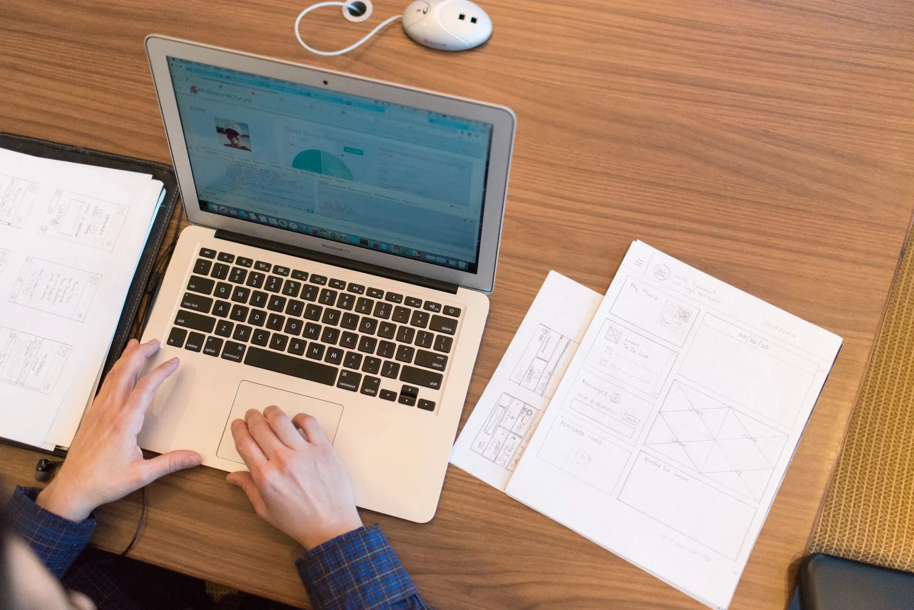 Personne travaillant sur un ordinateur portable entourée de maquettes d'interface dessinées à la main
