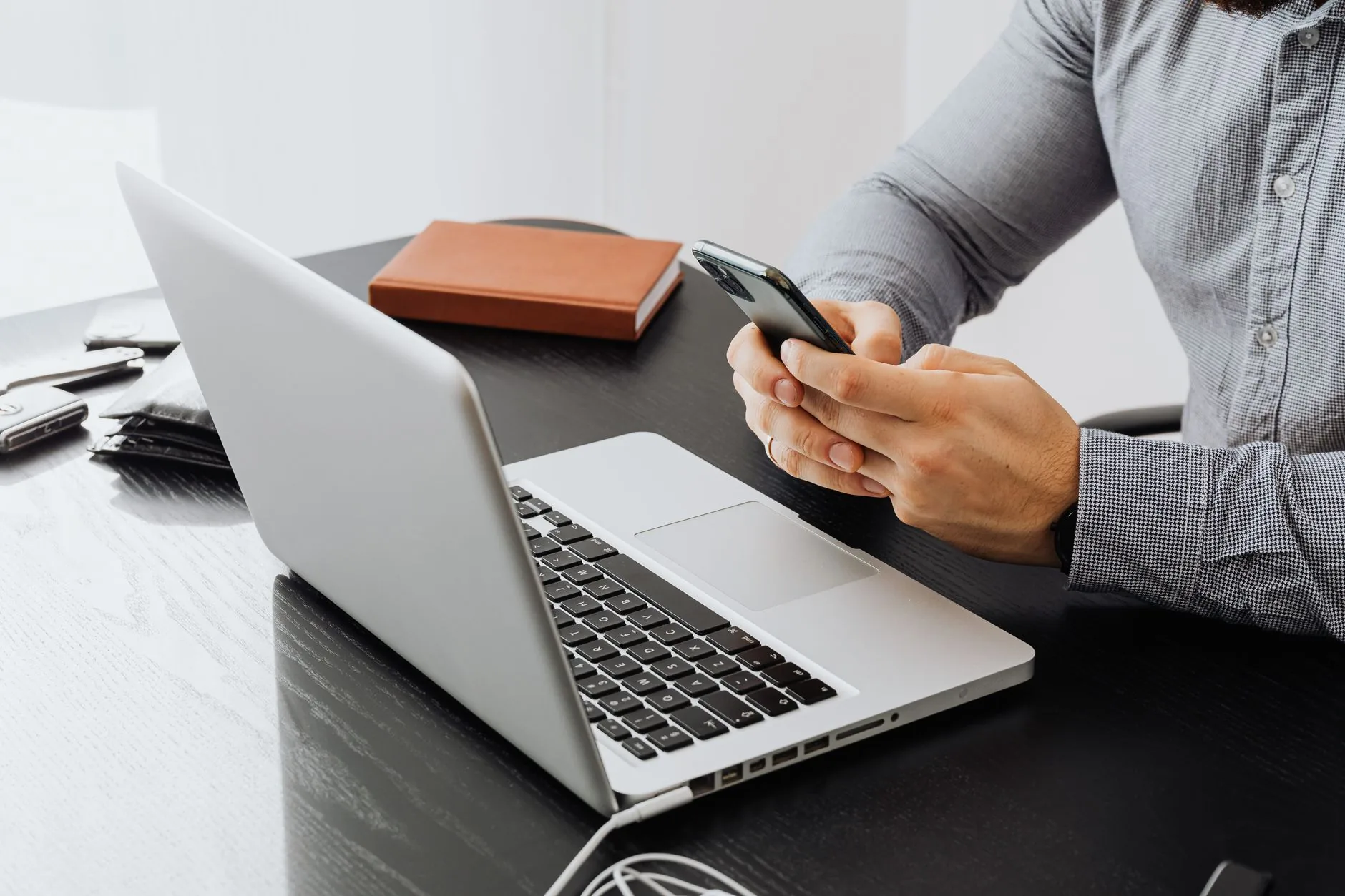 Personne tenant un smartphone devant un ordinateur portable ouvert sur un bureau