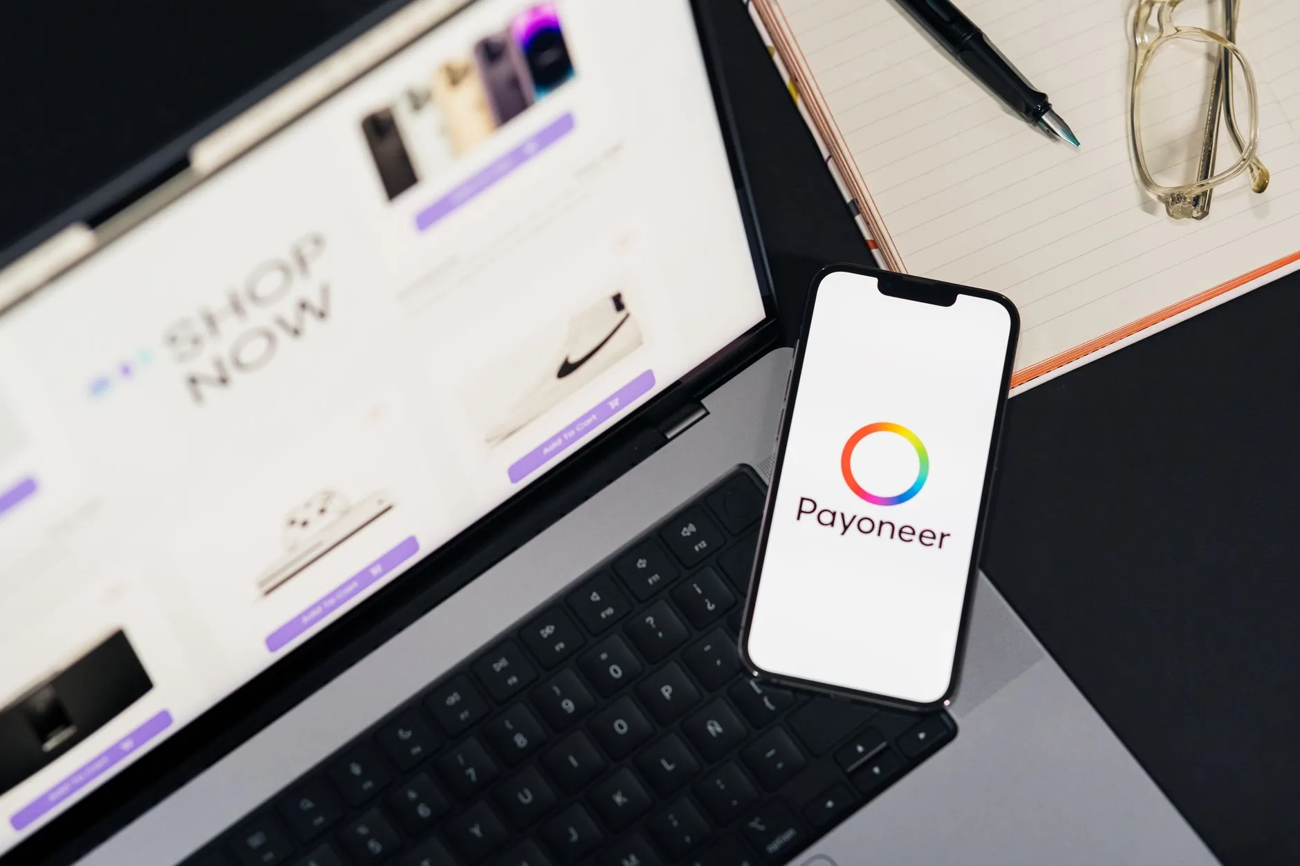 Smartphone affichant l'application Payoneer posé sur un ordinateur portable ouvert sur un site e-commerce